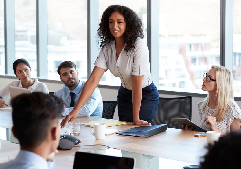 Businesswoman,Stands,To,Address,Meeting,Around,Board,Table Businesswoman,Stands,To,Address,Meeting,Around,Board,Table